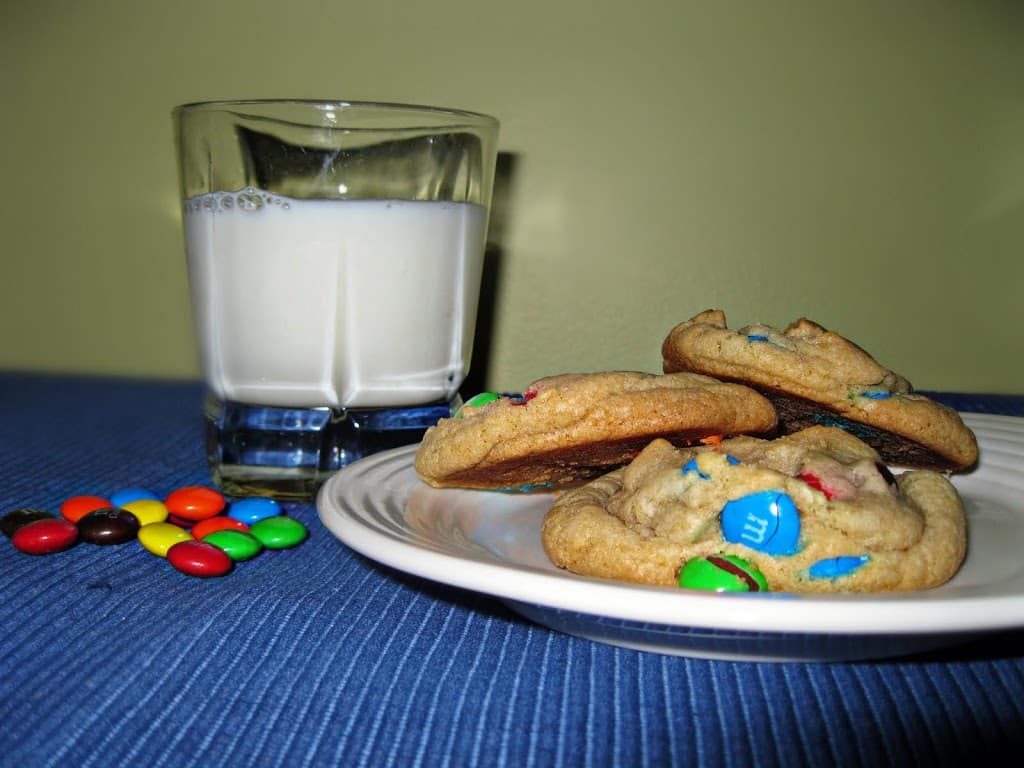 Side view of a few rainbow cookies on a white plate and a glass of milk on a table