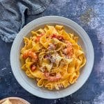 A white bowl of Crab & Shrimp Pasta with shredded cheese on top.