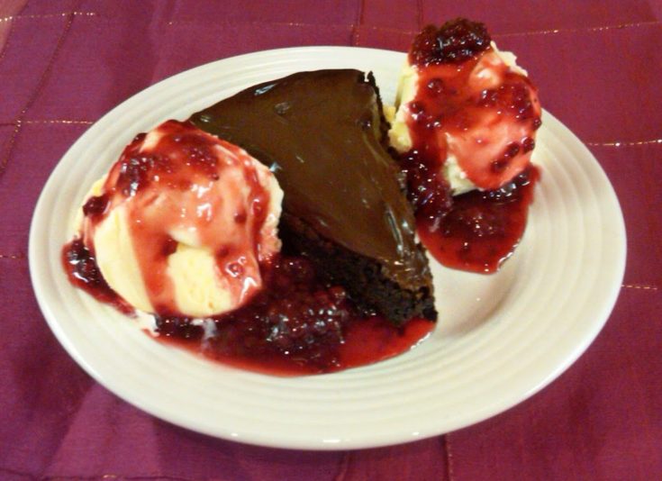 A slice of Flourless chocolate cake, and vailla ice cream topped with a raspberry sauce all on a white plate
