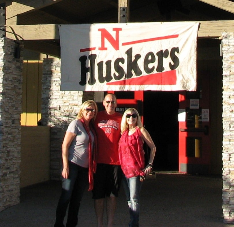 three fans standing outside huskers sign