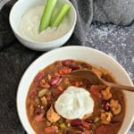 Slow Cooker Buffalo Chicken Chili in a white bowl and a side bowl of blue chese with celery sticks in it