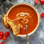Fire Roasted Tomato soup with a grilled cheese sandwich halved and a spoon in a white bowl.