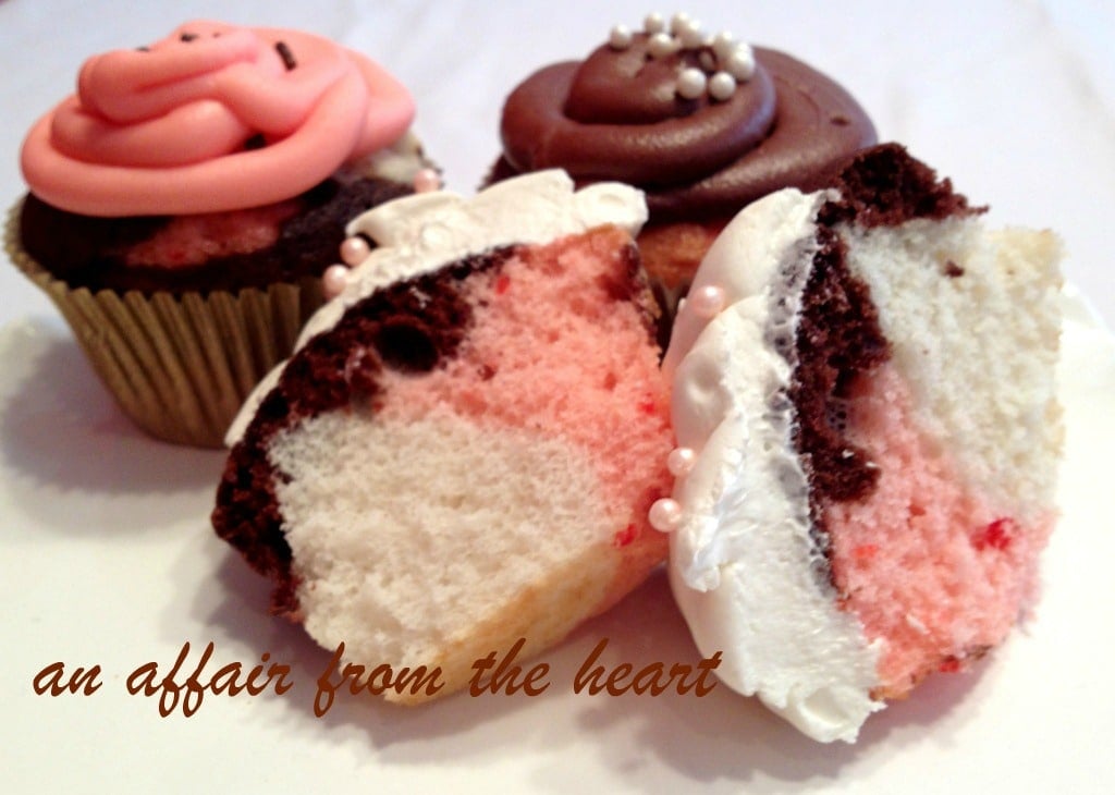 Neapolitan Cupcakes and one cut in half on a white surface