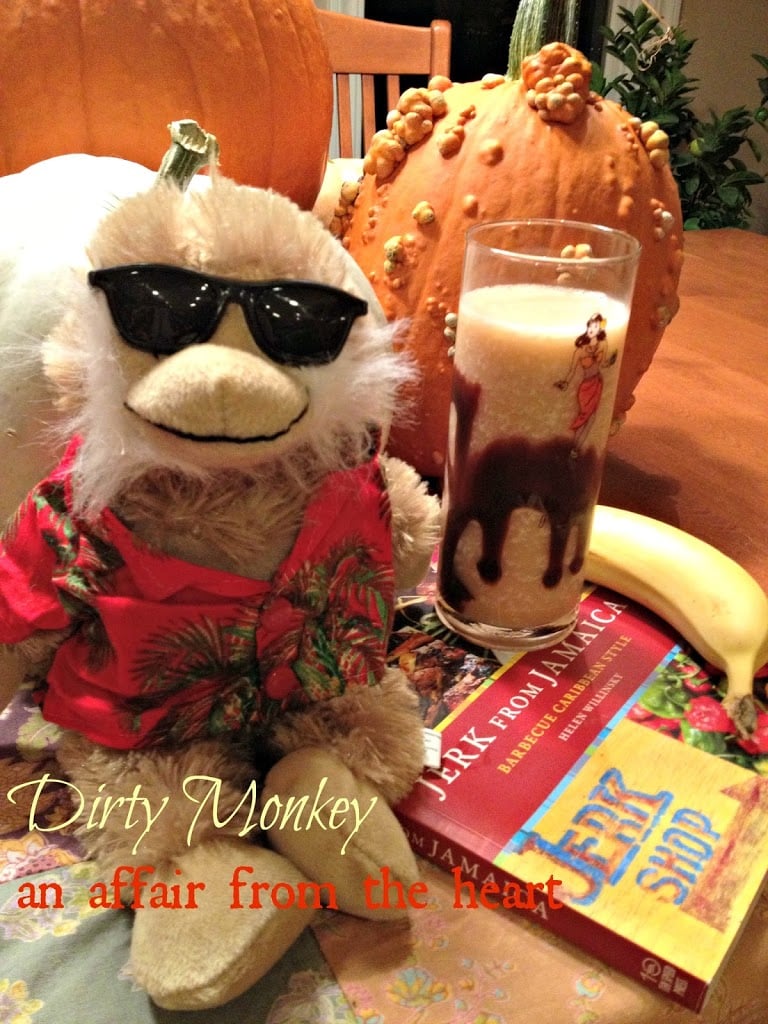 Dirty monkey cocktail with a stuffed monkey, a banana and a book on a table with text "dirty monkey"