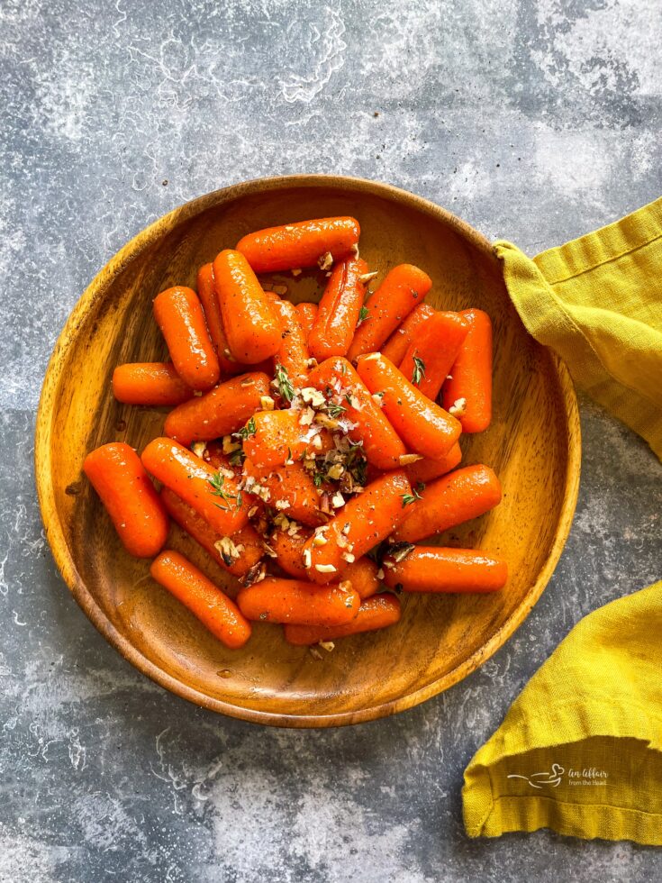 overhead of orange glazed baby carrots on a wooden plate.