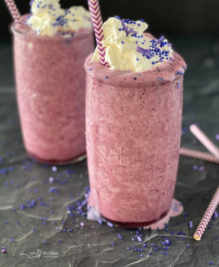 Two glasses of purple cow smoothie will whipped cream and sprinkles