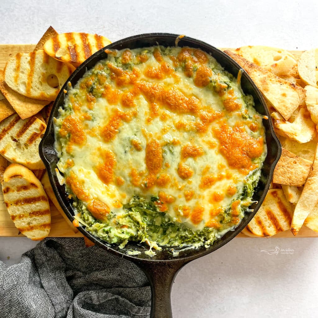 Spinach artichoke dip in a skillet surrounded by grilled bread.