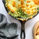 Close up of Spinach artichoke dip in a skillet surrounded by grilled bread.