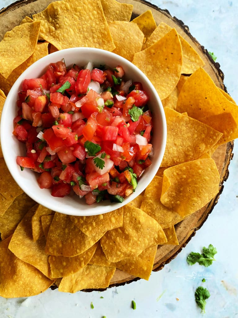 Pico de Gallo in a white bowl surrounded by tortilla chips