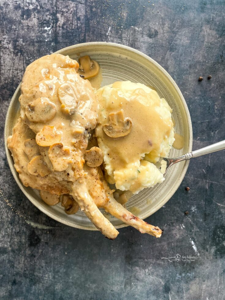 Pork chops with mushroom gravy, a fork and mashed potatoes on a cream color plate.