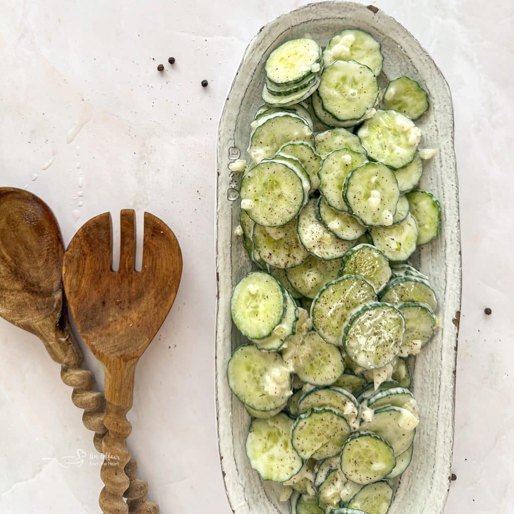 Cucumber Ranch Salad on a white serving dish and wooden salad serving spoons on a light colored table.