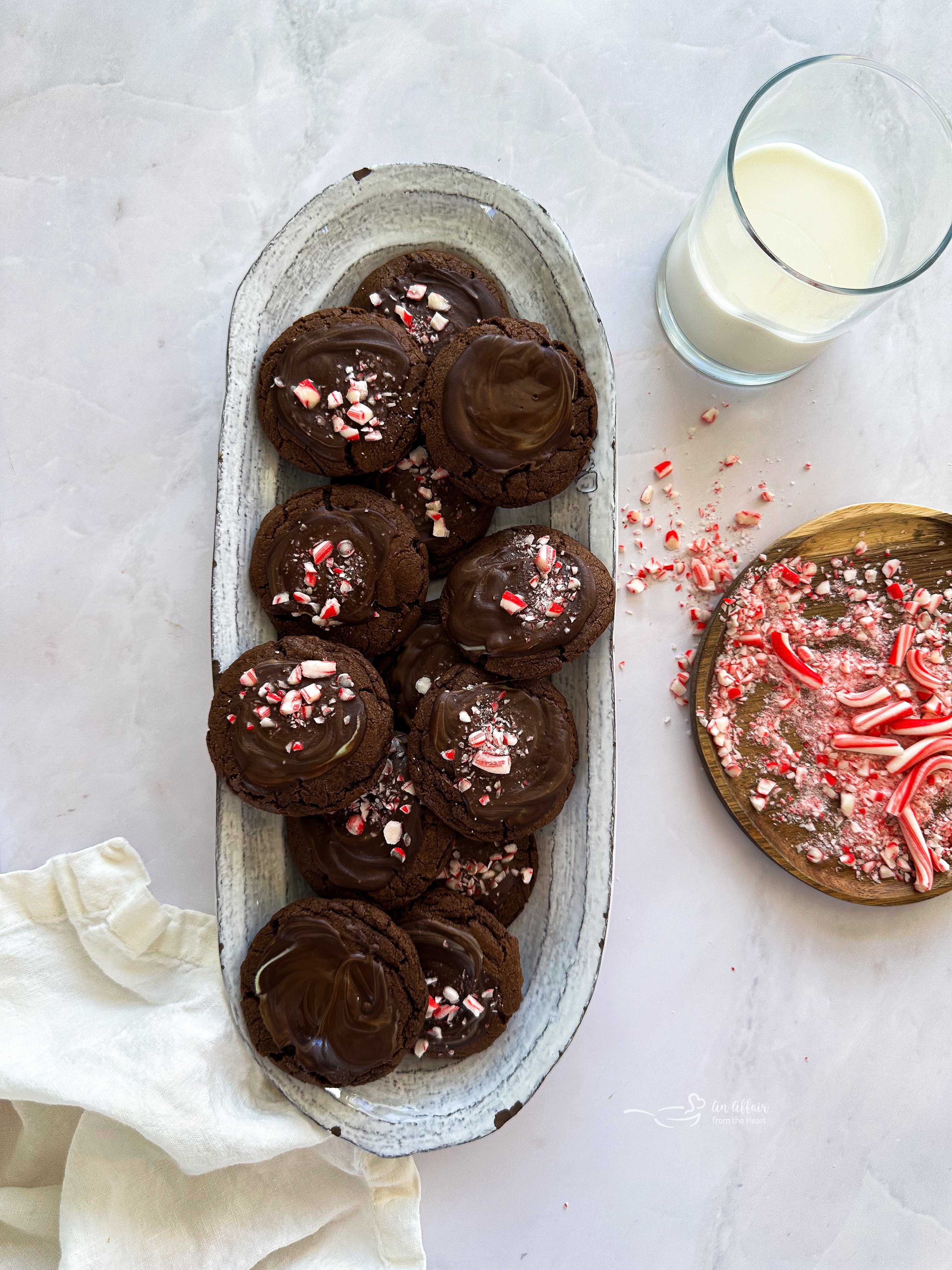 Chocolate Mint Candy Cookies on a serving platter next to a glass of milk and crushed candy canes.