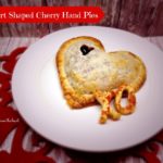 Heart shaped hand pie with pie crust piece XO on a white plate. Text "heart shaped cherry hand pies"