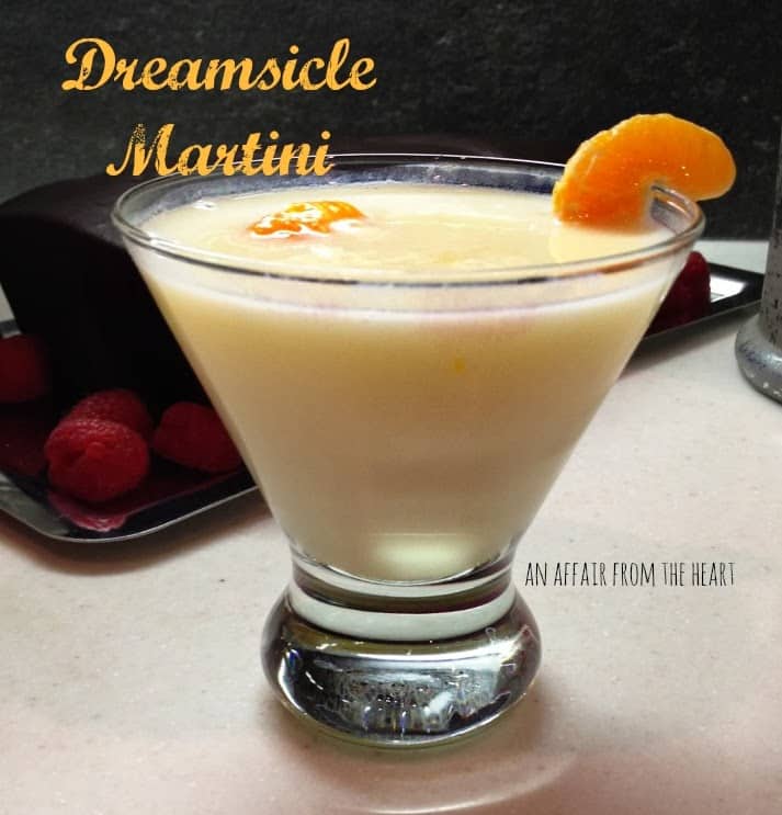 Dreamsicle martini in a martini glass garnished with an orange slice on a white surface. Text "dreamsicle martini"