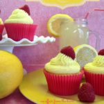 Side view Lemonade cupcakes on a yellow plate and on a white cake platter with half of lemons and a glass of lemonade on a pink surface. text "lemonade cupcakes with raspberry filling"