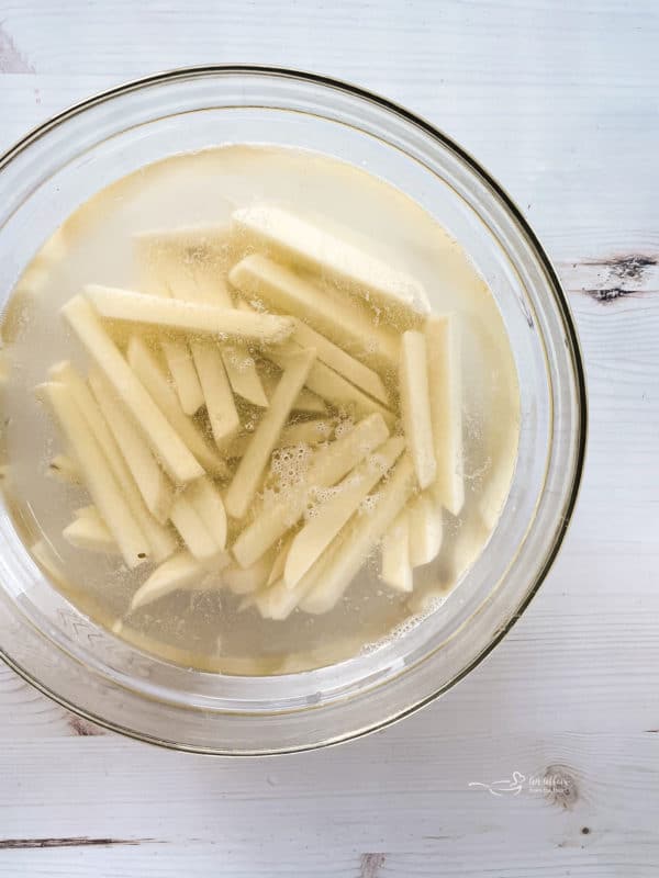 Bowl of peeled and cut fries in bowl of cold water