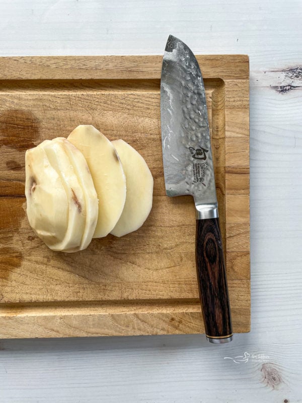 Top view of peeled sliced potato on wooden cutting board with knife