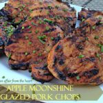Close up of pork chops on a white platter with text "Apple moonshine glazed pork chops"