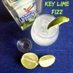 Overhead of key lime fizz, lime wedges, a shot glass and a bottle of Parrot Bay with text "Key LIme Fizz"