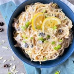 one bowl filled with pasta, tuna, mushrooms, olives, and lemon
