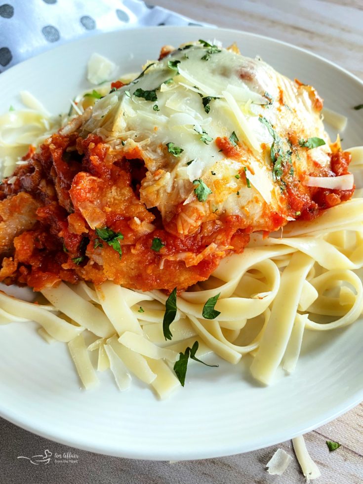 close view of chicken parmesan with tomato sauce and fresh parsley