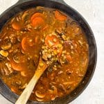 Stirring the Vegetable Beef Barley Soup with Mushrooms in the pot.