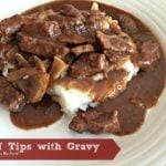 Beef Tips with Gravy over mashed potatoes on a white plate