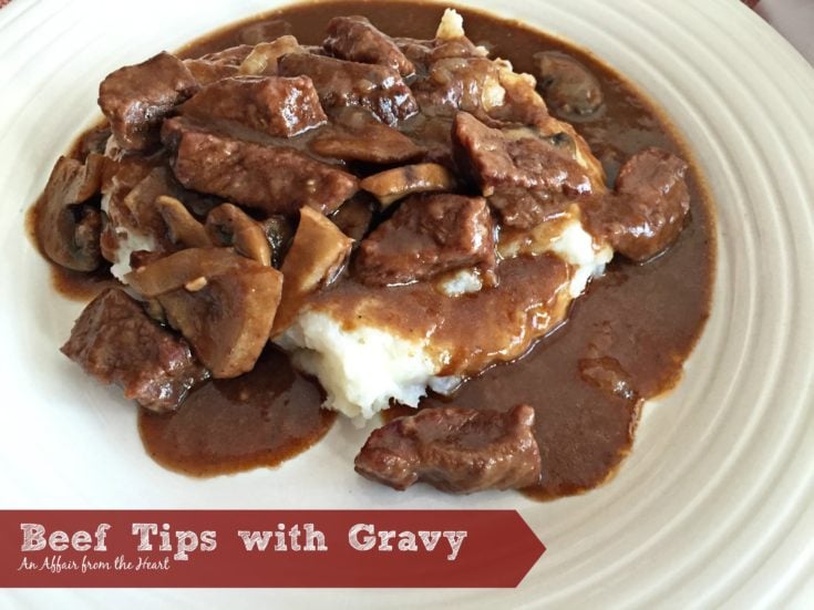 Beef Tips with Gravy over mashed potatoes on a white plate