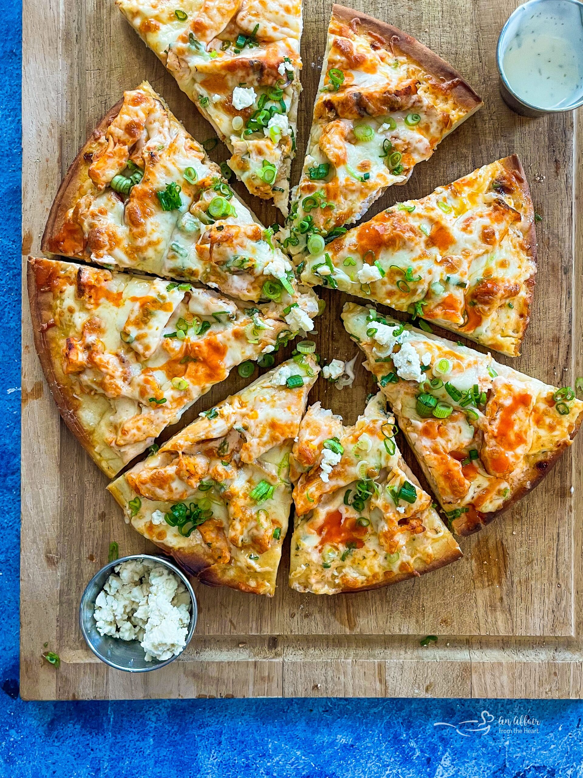 A sliced buffalo chicken pizza on a wood platter