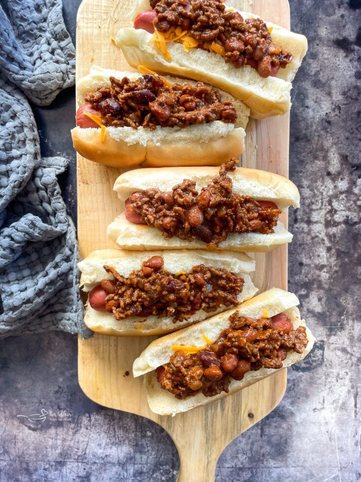 Hot dogs with chili on them on a wood board