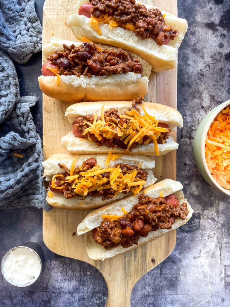 placing the cheese on top of the chili dogs