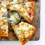 Reuben pizza sliced on a wood cutting board.