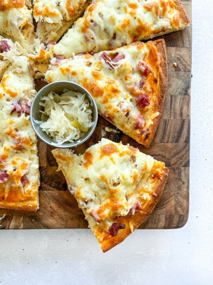 Reuben pizza sliced on a wood cutting board.