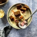 Cream of Reuben Soup in a green rimmed pottery bowl with rye croutons and spoonful of soup