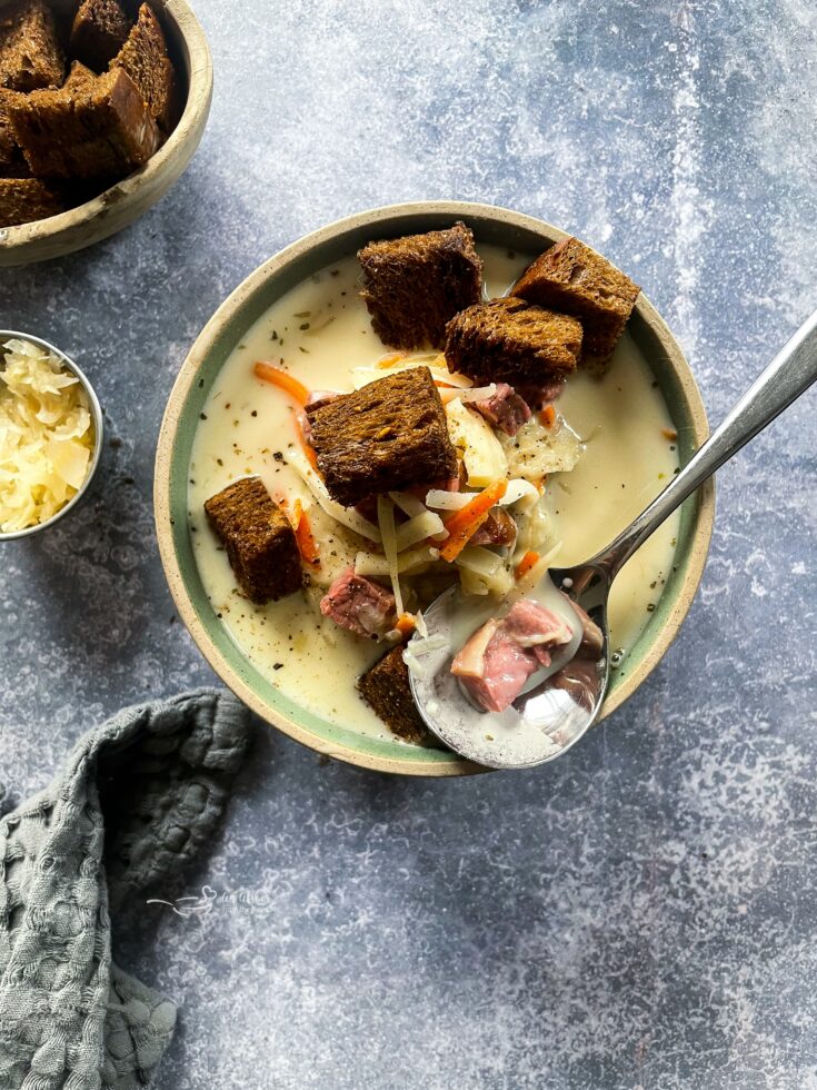 Cream of Reuben Soup in a green rimmed pottery bowl with rye croutons and spoonful of soup