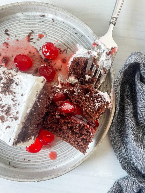 one slice of black forest cake on plate with white frosting and fork 