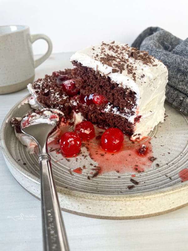 one slice of black forest cake on plate with Cool Whip and cherries