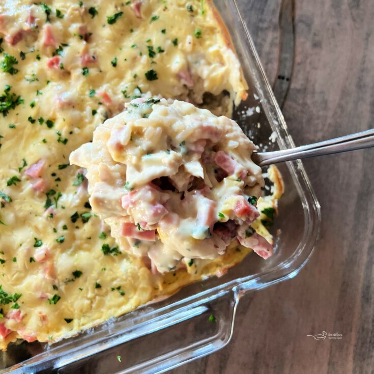 Scooping the Chicken Cordon Bleu Casserole with Rice out of a clear baking dish.