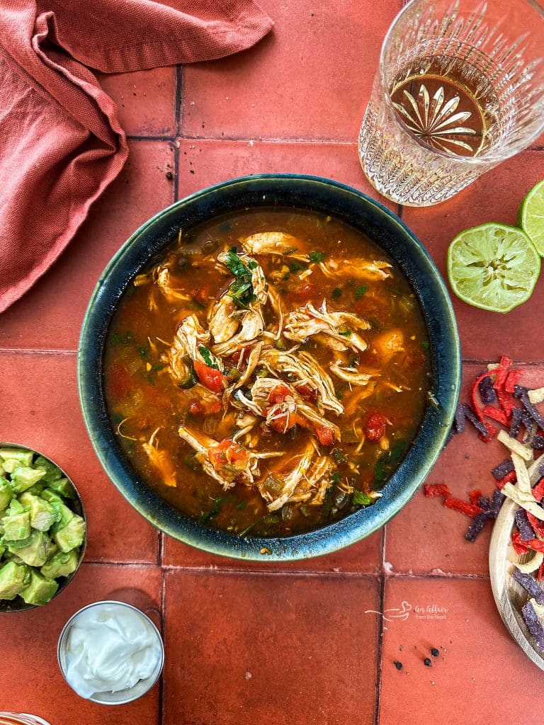 Bowl of Slow cooker Chicken Enchilada Soup with toppings on the side.
