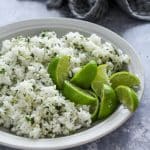 Cilantro Lime Rice and a hand full of quartered lime pieces in a white serving bowl.