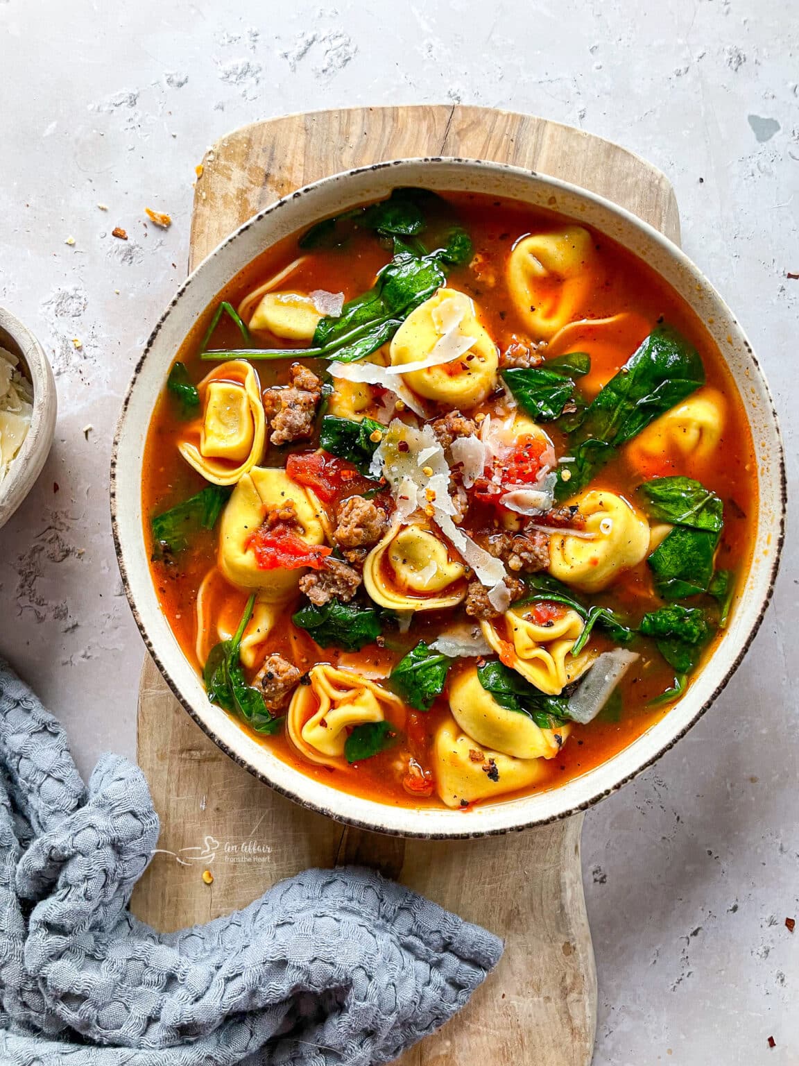 Top down view of a bowl of soup filled with ground sausage, tortellini, and spinach.