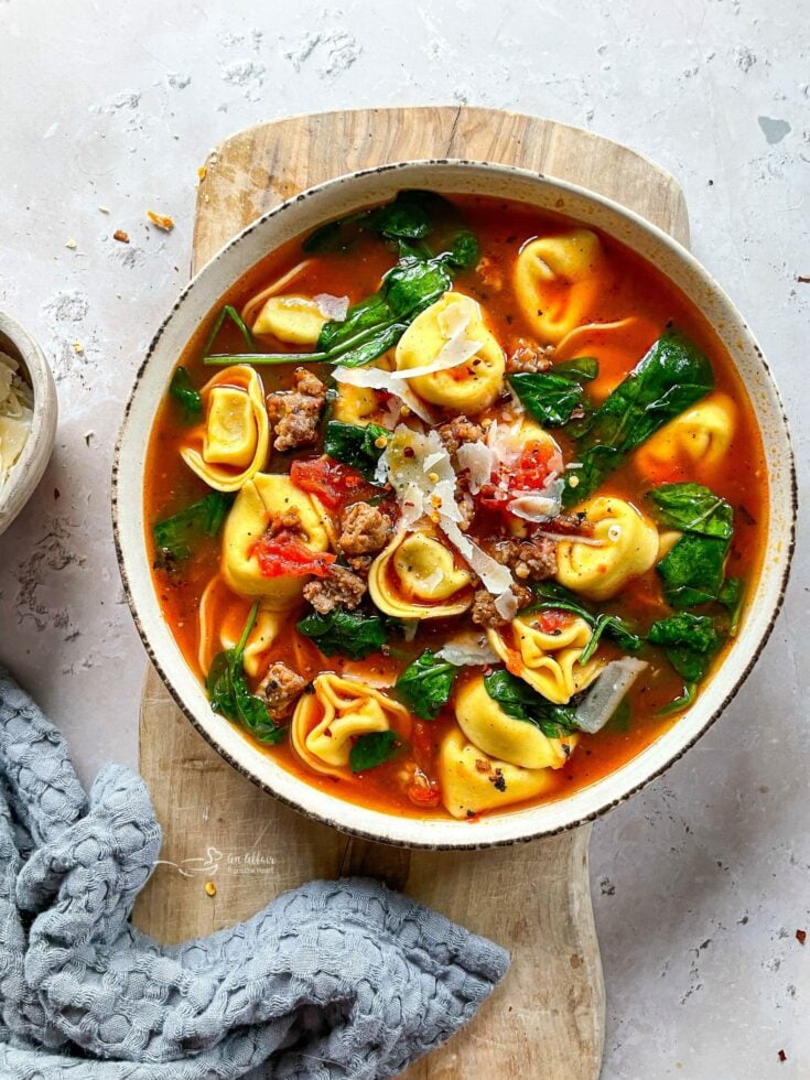 Close up of Tortellini soup with sausage in a white bowl.