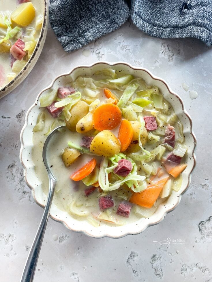 Creamy Corned Beef & Cabbage Soup in a white scallopped bowl with spoon