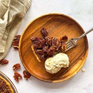 Close up of Slice of pecan pie, a fork and vanilla ice cream on a wooden plate