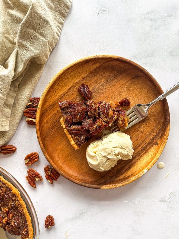 Close up of Slice of pecan pie, a fork and vanilla ice cream on a wooden plate