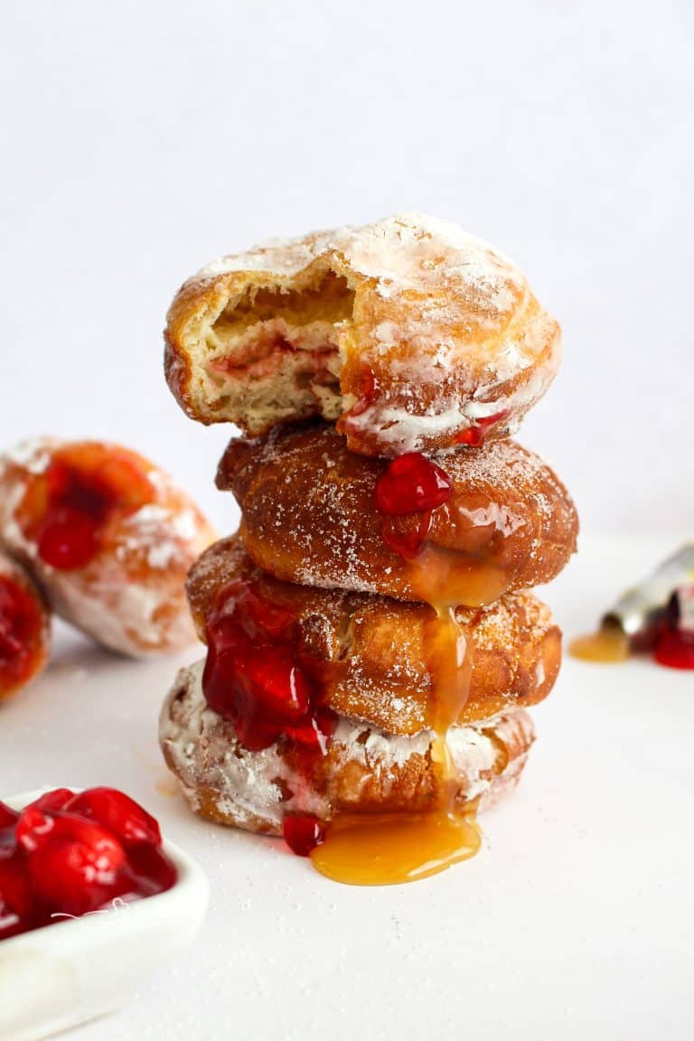 4 Pączki (Polish Donuts) stacked with the filling dripping out.