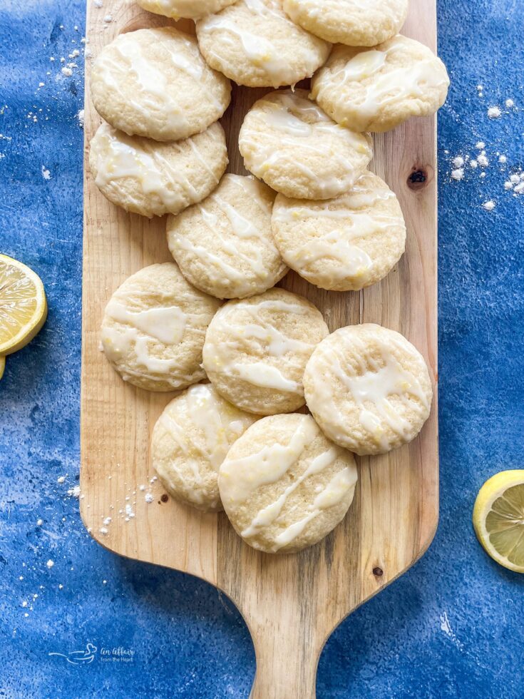 Glazed lemon cookies stacked on a wooden cutting board.