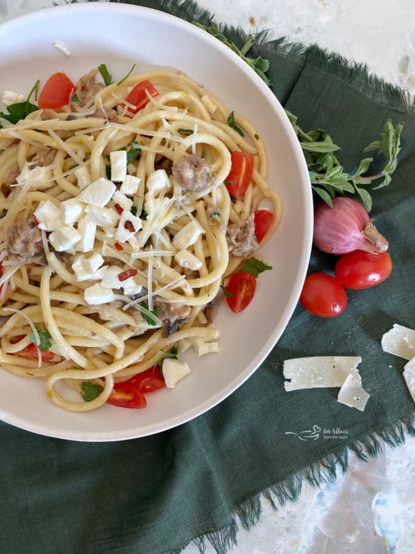 Top view of bucatini in a white bowl with tomatoes and mozzarella