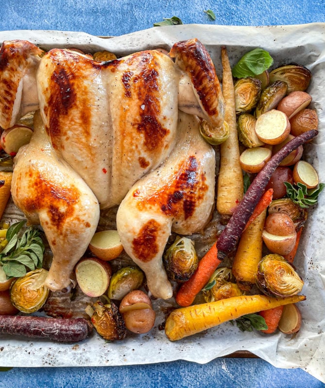 Top view of spatchcock chicken on baking sheet with carrots, potatoes, and Brussels sprouts