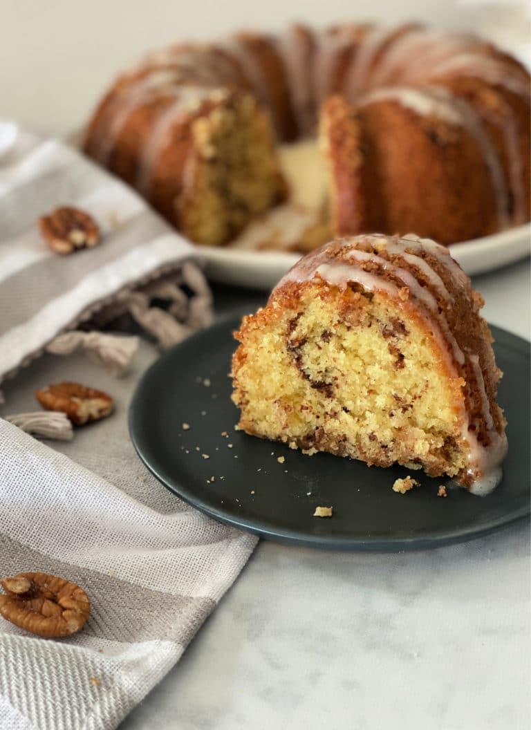 Sour Cream Coffee Cake slice on a dark plate with the rest of the cake in the background